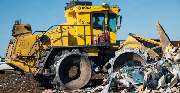 A yellow compactor flattening garbage of a sunny day. 
