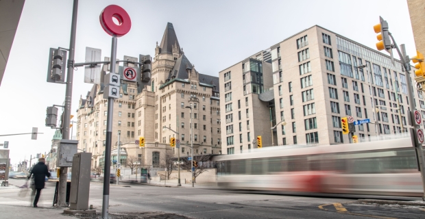 The corner of Rideau and Sussex with a moving bus, LRT sign post and the Chateau Laurier