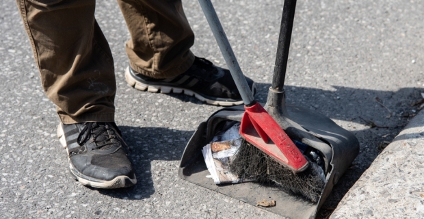 A worker sweeping litter from the street into a bucket dust pan