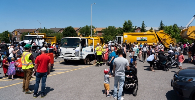 Adults accompany children in a parking lot displaying large trucks and equipment.  