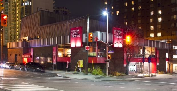 Exterior of Ottawa Little Theatre at night, showing dark brick facade with red feature panels. 