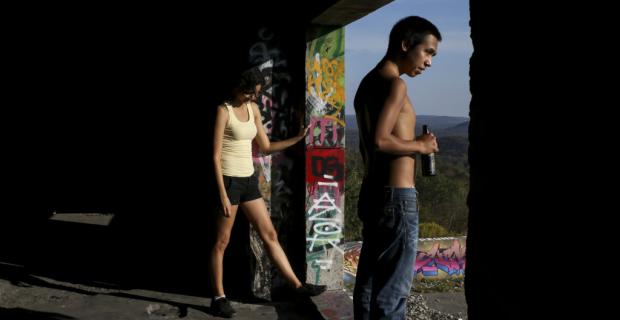 Photo of a young man and woman looking over a landscape through a graffitied doorway.