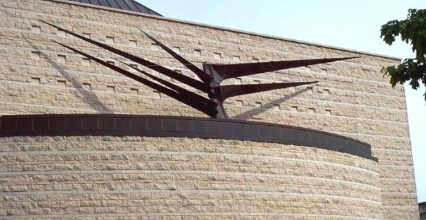 Abstract sculpture with large triangular metal branches extending from a central core on top of a building