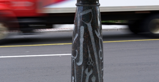 A bronze hat, parcel and envelope rest on a tray atop a marble column carved with silhouettes of the tools used in trades.