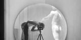 On aperçoit le reflet du photographe dans un miroir circulaire, l’appareil photo et le trépied étant au centre de l’œuvre. Le dos d’une sculpture figurative est également visible dans le reflet du miroir.
