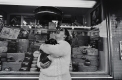 A black and white photograph of a woman who hugs her dog and looks upwards while laughing. The background is a storefront in Ottawa.