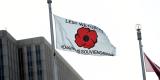 A white flag with the red poppy symbol and "Lest we forget" written in black text.