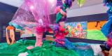 Une installation multicolore faite de tissus divers occupe un espace d’exposition. Des peintures couvrent le mur derrière l’installation.