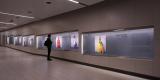 image shows an installation view of an exhibition in a long corridor; brightly coloured portraits of superheros hang in the vitrines.
