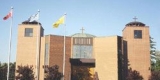 Grande église beige avec de larges marches avant. Trois croix se trouvent au sommet du bâtiment et trois grands mâts de drapeau sont assis parmi les arbres.
