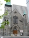 L’église avec un extérieur en pierre calcaire et de grandes portes d’entrée en bois est entourée de grands immeubles de bureaux au centre-ville d’Ottawa.