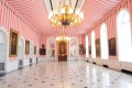 Tente avec murs et plafond à rayures roses et blanches. Portraits d'anciens gouverneurs généraux sur les murs. Deux lustres pendent du plafond.