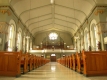 Intérieur de la cathédrale avec plafond blanc et murs gris avec des détails dorés. Un grand orgue se trouve à l’arrière devant une grande fenêtre. 