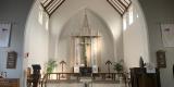 A large chancel with white walls, high ceilings and wooden beam. Natural light pours in from four high windows. 