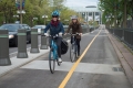 Deux cyclistes souriants empruntent la piste cyclable de l’avenue Mackenzie, avec le Musée des beaux-arts du Canada en arrière-plan.