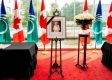 Picture of Queen with a black ribbon on the frame beside a bouquet of flowers surrounded by flags