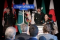 Speaker at podium speaking with soldiers standing beside commemorative street sign and flags in background