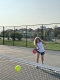 Luisa joue au pickleball sur un terrain de tennis extérieur qui jouxte un parc arboré en arrière-plan.