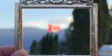 Un drapeau canadien flottant dans un paysage montagneux, encadré au premier plan par un cadre traditionnel chinois tenu par le photographe.