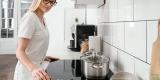 Woman turning off the stove burner with a pot covered on the stove top.