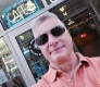 Photo d'un homme en lunettes de soleil prenant un selfie devant un petit commerce.