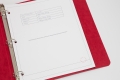 A three-ring, red binder is open and showing white paper in the binder. 