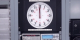 A video still of a clock, with its hands pointing to twelve. Various buttons and screens are below the clock. Text above the clock reads “National Research Council of Canada”
