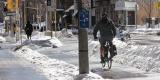 Un cycliste circule sur une piste cyclable près d’une rue urbaine en hiver.