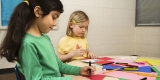 Two young girls sitting at a table while doing arts and crafts.