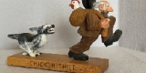 Humorous hand carving of a dog chasing a man clutching a chicken in a sack thrown over his shoulder.