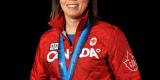 Headshot of Coach Carla MacLeod with an Olympic gold medal. She is wearing a red zip-up sweater with “Canada” written across the chest. 