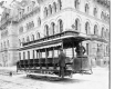 Open streetcar with conductor onboard in front of building