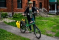 Un cycliste portant un casque se tient avec sa bicyclette devant sa maison.