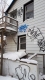 A white two-storey house with broken windows and problem graffiti sprayed over it in five areas.