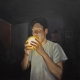A striking oil on canvas painting of a young man in a dark room, holding a glowing orb near his mouth.