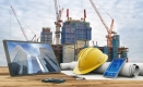 Écran d’ordinateur, téléphone et tablette avec casque de chantier, papier à dessin et bâtiment en construction.