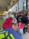 Woman in red cape handing out reflective arm bands to children in costumes/Une femme en cape rouge distribue des brassards réfléchissants à des enfants déguisés.