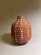 A hand built, clay vase with many small faces rendered simply in white, black and red glaze on the natural clay colour.