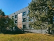 Le mur extérieur du bâtiment de trois étages est situé derrière des arbres et une clôture de construction lors d’une journée claire et ensoleillée.