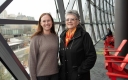 Raynor Boutet and Mary D’Aoust stand side by side in front of a glass facade with the parliament buildings in the background.