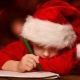 child wearing a santa hat while writting a letter