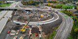 Aerial photograph with highway 417 on the left and Pinecrest interchange ramp construction in the centre with poured concrete curbs and a large yellow crane working on the guideway trench.